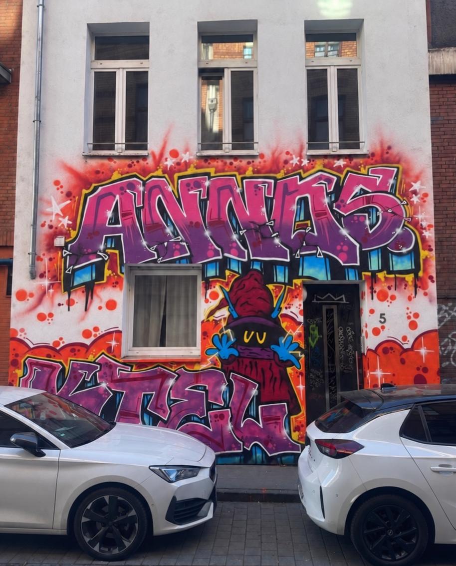 Fassadengestaltung mit großem pinkem Graffiti-Schriftzug und Figur an einem Altbau